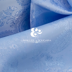 May include: A close-up of a light blue fabric with a white paisley pattern. The fabric is folded in half, and the text "LAVAILLER & BOUGARA" is visible in the center of the image.