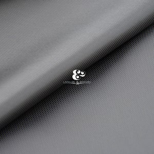 May include: A close-up of a grey, textured fabric with a subtle pattern. The fabric is folded in half, revealing a lighter grey underside. The fabric is labelled "LAVALLIER & BOUCHARA"