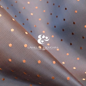 Puede incluir: Primer plano de una tela azul con un patrón de lunares color cobre. La tela está doblada, creando sombras y reflejos. El texto "LAVAILLE & BOUGARA" es visible en la esquina inferior derecha.