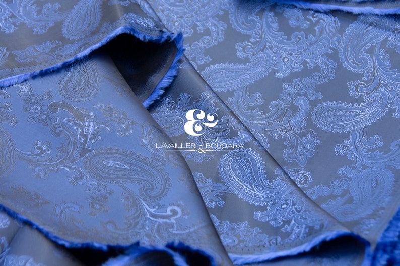 May include: Blue paisley patterned fabric with a white paisley design. The fabric is folded and the edges are frayed. The text "LAVAILLEUR & BOUJARA" is visible in the center of the image.