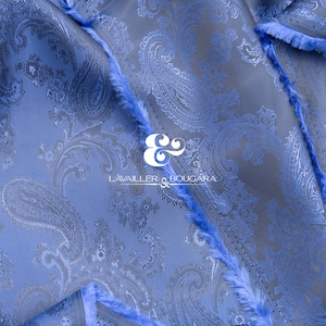 May include: Blue paisley patterned fabric with a frayed edge. The fabric has a subtle sheen and a soft texture. The fabric is labeled "LAVAILLEUR & BOUGARA" in black text.