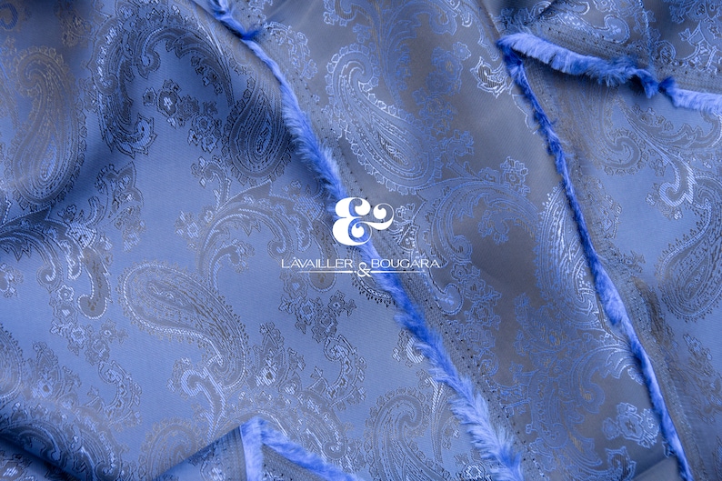 May include: Blue paisley patterned fabric with a frayed edge. The fabric has a subtle sheen and a soft texture. The fabric is labeled "LAVAILLEUR & BOUGARA" in black text.