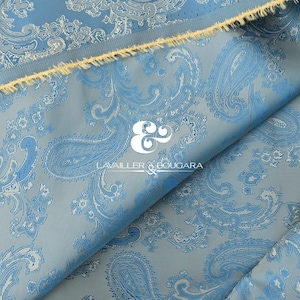 May include: A folded piece of light blue fabric with a paisley pattern in a lighter shade of blue. The fabric has a raw edge with a yellow fringe. The logo "LAVAILLER & BOUGARA" is visible.