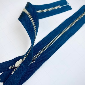 May include: A blue zipper with silver teeth. The zipper is open and the slider is visible.