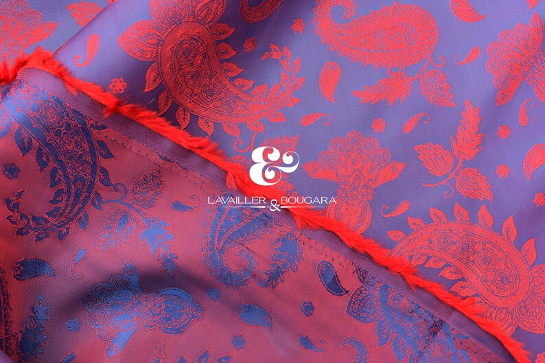 Puede incluir: Primer plano de una tela con un estampado de cachemir en tonos morados, rojos y azules. La tela tiene un aspecto texturizado y un borde con flecos. El texto "LAVALLER & BOUGARA" es visible.