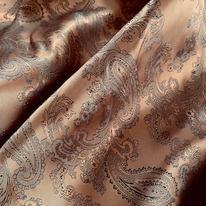 以下が含まれることがあります： ペイズリー柄の茶色の布のクローズアップ。布は控えめな光沢と柔らかな質感があります。