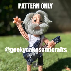 May include: A crocheted doll of an elderly man with grey hair and beard, wearing a white shirt, dark trousers, and a denim guitar. The doll is holding the guitar and has its arm raised. The text "PATTERN ONLY" is at the top.