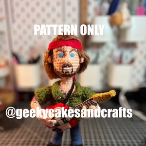 May include: Crocheted amigurumi doll of a musician with a red bandana, green shirt, and blue jeans, holding a red and gold electric guitar. The doll has a beard and blue eyes. The text "PATTERN ONLY" is at the top of the image and "@geekycakesandcrafts" is at the bottom.