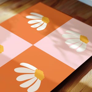 May include: A close-up of a patterned surface with a checkerboard design. The squares alternate between orange and pink, each featuring a white daisy with a yellow center. The image is angled, showing the pattern's details.