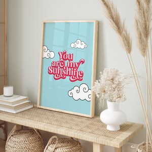May include: A framed print with a blue background and white clouds. The text "You are my sunshine" is written in pink and red letters.