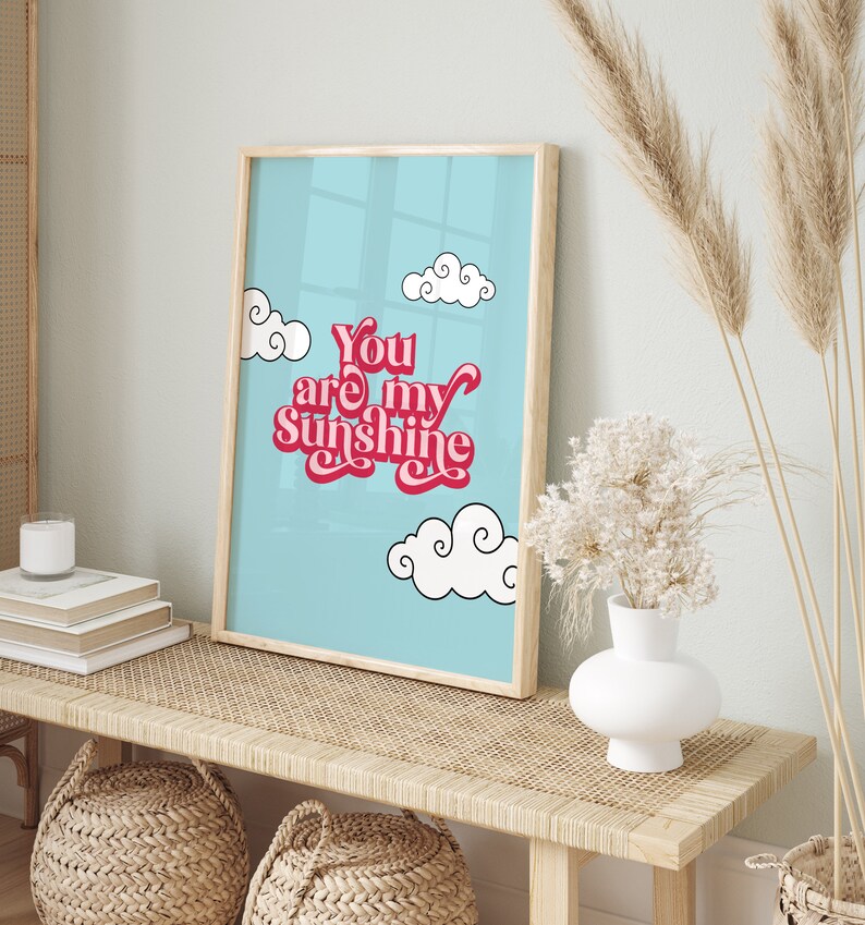 May include: A framed print with a blue background and white clouds. The text "You are my sunshine" is written in pink and red letters.
