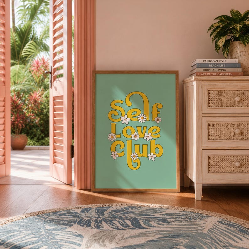 May include: A framed wall art print featuring the text Self Love Club in a yellow, rounded, retro-style font on a sage green background, decorated with small white daisy flowers with yellow centres, displayed in a wooden frame.