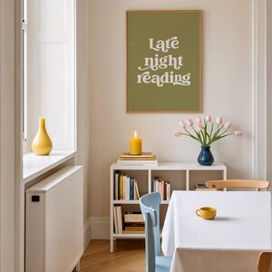 May include: A dining room scene featuring a framed print with the text "Late night reading" above a white shelf with books, a lit candle, and a blue vase of pink tulips. A yellow cup sits on a white tablecloth.