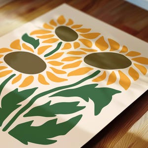 May include: A print featuring three stylized sunflowers with yellow petals and brown centers. Green leaves and stems are visible against a cream background. The artwork has a modern, minimalist aesthetic, suitable for home decor.
