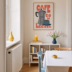 May include: A dining room scene featuring a framed poster with the words "CAFE CON LECHE" and a coffee pot illustration. A white table is set with a white tablecloth and a yellow cup. A blue vase holds pink tulips, and a yellow candle burns on a shelf.