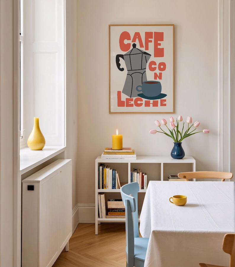 May include: A dining room scene featuring a framed poster with the words "CAFE CON LECHE" and a coffee pot illustration. A white table is set with a white tablecloth and a yellow cup. A blue vase holds pink tulips, and a yellow candle burns on a shelf.