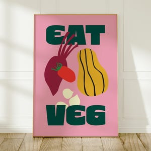 Könnte beinhalten: Ein rechteckiger Wandkunstdruck mit rosa Hintergrund und dem dunkelgrünen Text EAT VEG. Das Design zeigt eine dunkelrote Rote Bete, eine rote Tomate, einen gelben Butternusskürbis mit schwarzen Umrissen und drei kleine cremeweiße Knoblauchzehen.