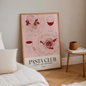 K&ouml;nnte beinhalten: Gerahmtes Poster mit rosa Hintergrund, das Strichzeichnungen von Pastagerichten und Weingl&auml;sern zeigt. Der Text "PASTA CLUB" steht unten, darunter "EAT DAILY - SERVE WITH CHEESE". Das Poster wird in einem Raum mit Bett und Beistelltisch angezeigt.
