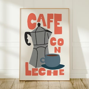 May include: A framed art print with a coffee theme. The print features a gray stovetop espresso maker, a blue cup and saucer, and the words "CAFE CON LECHE" in coral-colored block letters. The background is off-white.