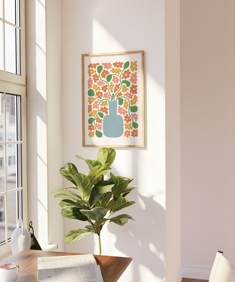 May include: A framed art print featuring a stylized floral arrangement. The artwork showcases a light blue vase filled with orange, yellow, and pink flowers with green stems and leaves. The print is set against a white background and framed in a light wood.