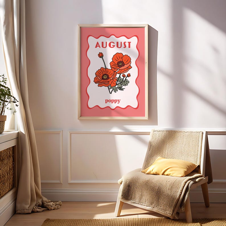 May include: A framed art print featuring a stylized illustration of red poppies. The print has a pink background with the word "AUGUST" at the top and "poppy" at the bottom. The frame is light wood.