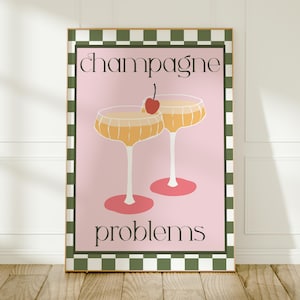 May include: Framed art print with a pink backdrop, two champagne glasses, and a cherry. The words "champagne problems" are written in a stylish font. The frame has a green and white checkered border.