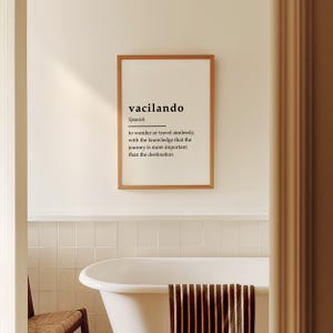 Puede incluir: Una impresi&oacute;n enmarcada con la palabra espa&ntilde;ola "vacilando" y su definici&oacute;n: "vagar o viajar sin rumbo, con el conocimiento de que el viaje es m&aacute;s importante que el destino". La impresi&oacute;n est&aacute; colgada en una pared de azulejos blancos en un ba&ntilde;o.