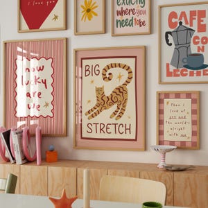 May include: A collection of framed art prints with various designs and text. One print features a cat with the words "BIG STRETCH." Other prints include phrases like "I love you," "How lucky are we," and "Cafe con Leche."