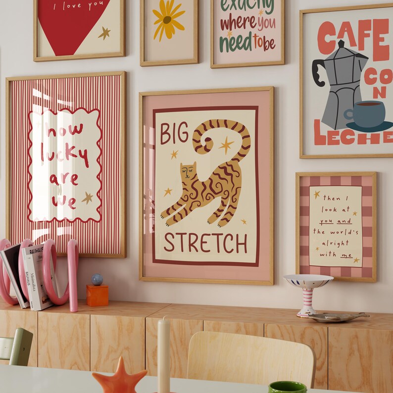 May include: A collection of framed art prints with various designs and text. One print features a cat with the words "BIG STRETCH." Other prints include phrases like "I love you," "How lucky are we," and "Cafe con Leche."