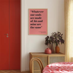 Op de afbeelding: Een rechthoekige wandkunstprint in een lichthouten lijst met een zalmroze achtergrond en zwarte tekst die luidt: "Whatever our souls are made of, his and mine are the same" gevolgd door "WUTHERING HEIGHTS EMILY BRONT&Euml;".