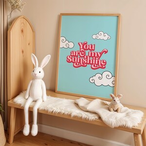 May include: A framed print with a blue background and white clouds. The print features the text "You are my sunshine" in red and pink letters.