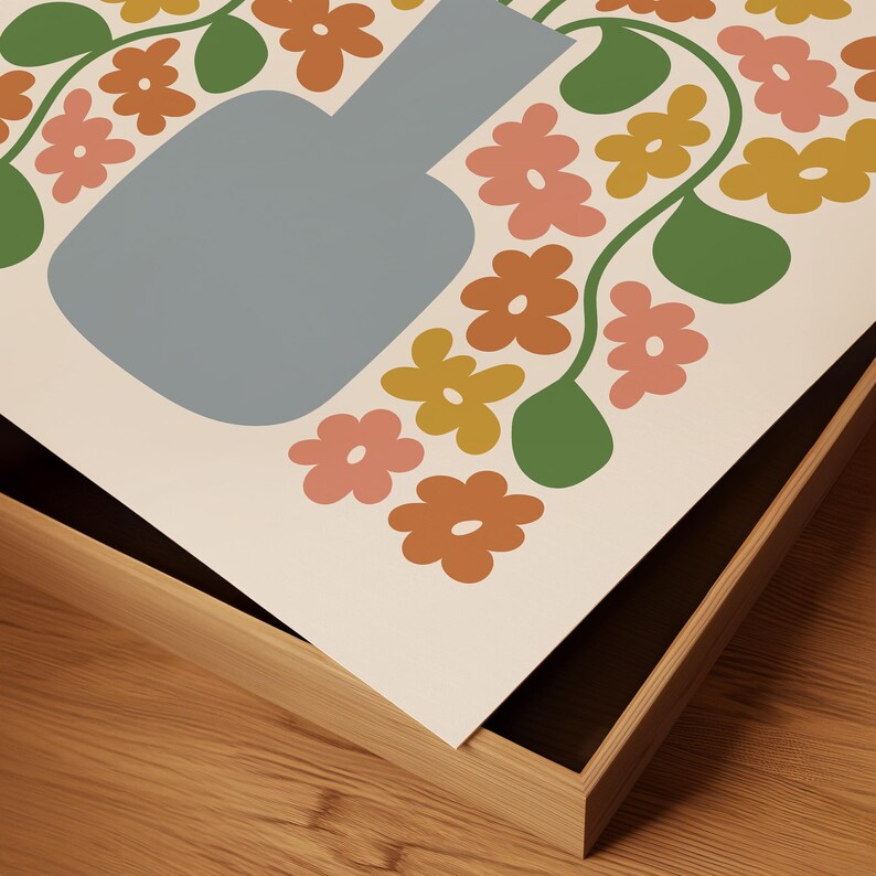May include: A framed art print featuring a stylized floral design. The artwork showcases a light blue vase surrounded by flowers in shades of orange, pink, and yellow, with green leaves. The print is set against a cream background and framed in a light wood.