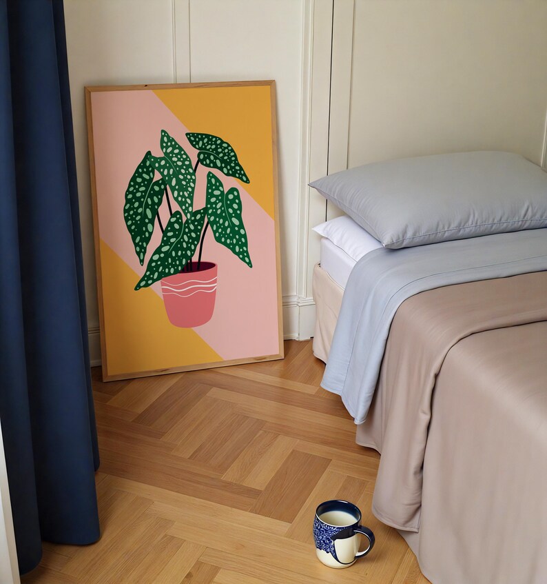 May include: A framed botanical print of a green plant with white spots in a pink pot, set against a yellow and pink geometric background. A bed with grey and beige bedding and a blue and white patterned mug are also visible.