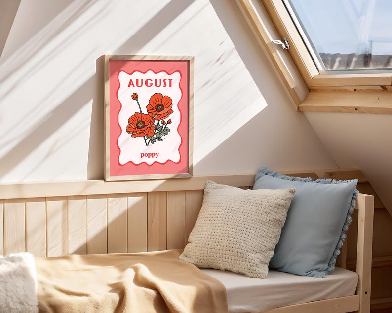 May include: A framed art print featuring a poppy flower illustration. The artwork has a pink background with the word "August" at the top and "poppy" at the bottom. The frame is made of light-colored wood.