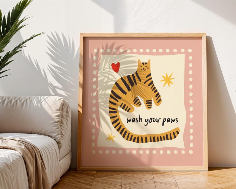 K&ouml;nnte beinhalten: Ein quadratischer Wandkunstdruck in einem Rahmen, der einen stilisierten orangefarbenen Tiger mit schwarzen Streifen auf cremefarbenem Hintergrund zeigt. Das Bild enth&auml;lt ein kleines rotes Herz, zwei gelbe Sterne und den schwarzen Text "wash your paws".