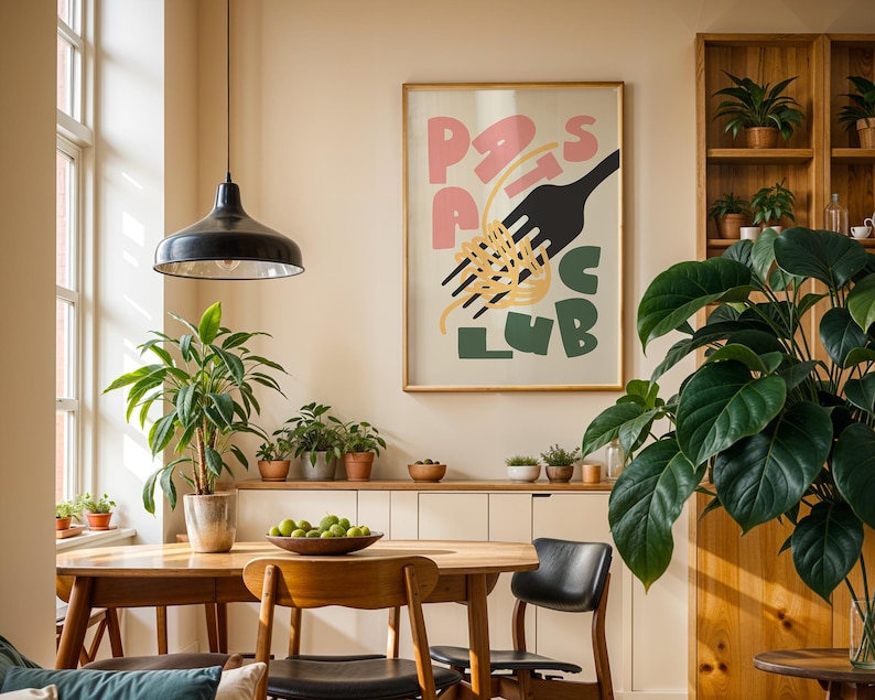 May include: A dining room scene featuring a wooden table and chairs, a large framed poster with the words "Pasta Club", and several potted plants. A black pendant light hangs above the table, and a wooden cabinet with plants sits in the background.