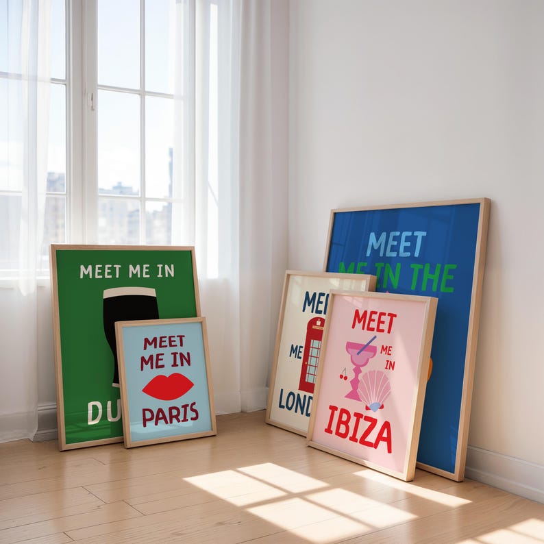 May include: A collection of framed travel-themed art prints. The prints feature phrases like "Meet Me In Paris," "Meet Me In London," and "Meet Me In Ibiza," with colorful graphics and text on a white wall.