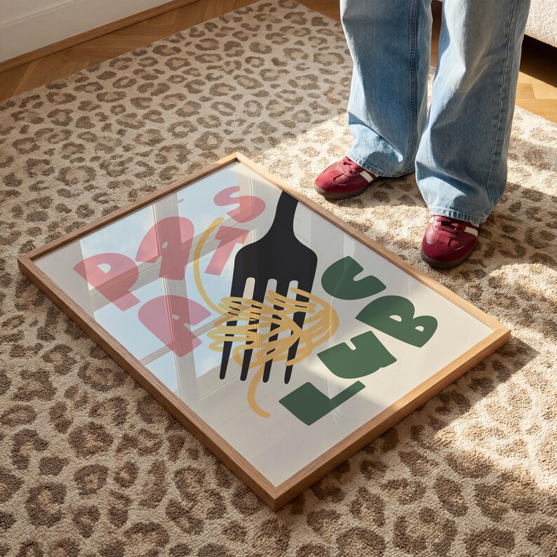 May include: A framed art print featuring a black fork, yellow spaghetti, and the words "Pasta Love" in pink and green. The artwork is displayed on a leopard print rug, with a person wearing blue jeans and red shoes standing nearby.