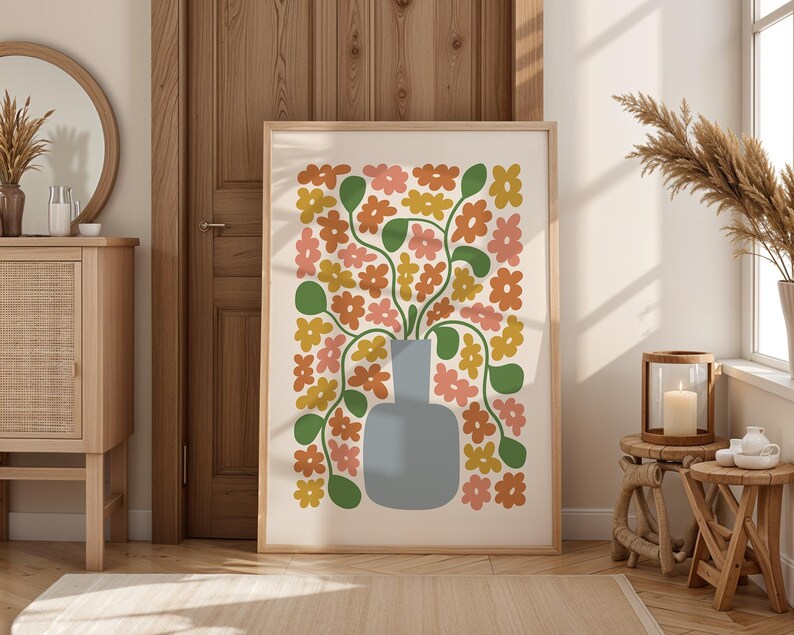 May include: A framed floral art print featuring a vase with colorful flowers in shades of orange, pink, and yellow. The vase is a light blue color. The artwork is displayed in a light wood frame.