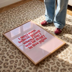 K&ouml;nnte beinhalten: Ein rechteckiges gerahmtes Wandbild mit hellrosa Hintergrund und fettgedrucktem rotem Text: I don't even believe myself when I say I will be ready in five mins. Der Rahmen besteht aus hellem Holz und hat eine reflektierende Glasoberfl&auml;che.