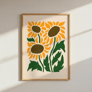 May include: A framed art print featuring a stylized illustration of sunflowers. The artwork showcases three sunflowers with yellow petals and brown centers, set against a cream background. Green leaves and stems complete the floral design.