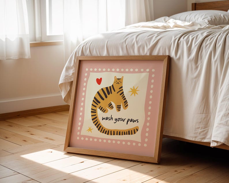 K&ouml;nnte beinhalten: Ein quadratisches gerahmtes Wandbild mit einem hellrosa Rand und wei&szlig;en Punkten. In der Mitte ist ein gelber Tiger mit schwarzen Streifen, ein kleines rotes Herz, zwei gelbe Sterne und der schwarze Text "wash your paws" zu sehen.
