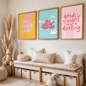 May include: Three framed prints with colorful backgrounds and white text. The prints are hanging on a white wall above a wooden bench with storage bins. The prints read "There is power in kindness", "You are my sunshine", and "Good night my darling".