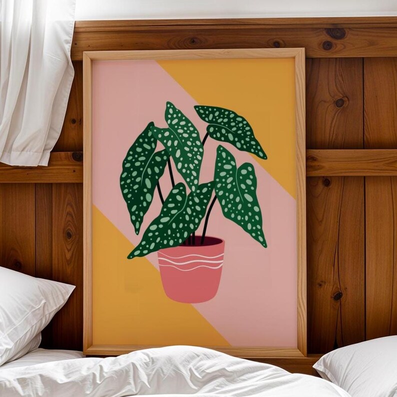 May include: A framed art print depicting a stylized plant illustration. The plant has large, green leaves with white spots, and is potted in a pink pot with white stripes. The background is a geometric design in pink and yellow.