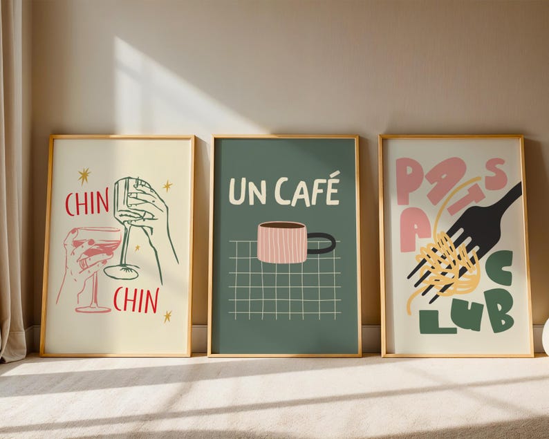 May include: Three framed art prints with gold frames. The prints feature illustrations of wine glasses, a coffee cup with the text "UN CAF&Eacute;", and pasta with a fork. The prints are in a modern, minimalist style.
