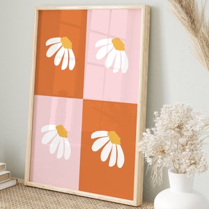 May include: A framed art print featuring a daisy design. The artwork is divided into four squares, alternating between orange and pink. Each square has a white daisy with a yellow center. The frame is light wood.