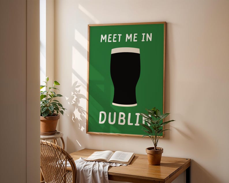 May include: A framed poster with a green background and the words "MEET ME IN DUBLIN" in white. A black pint of stout with a white head is centered on the poster. The poster is displayed on a wall above a wooden desk.
