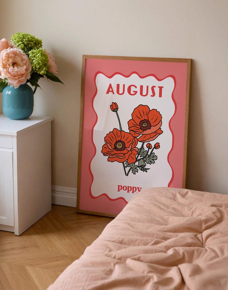May include: A framed art print featuring a pink background with a white, wavy-edged center. The print displays the word "AUGUST" in red, along with illustrations of orange poppies and the word "poppy".
