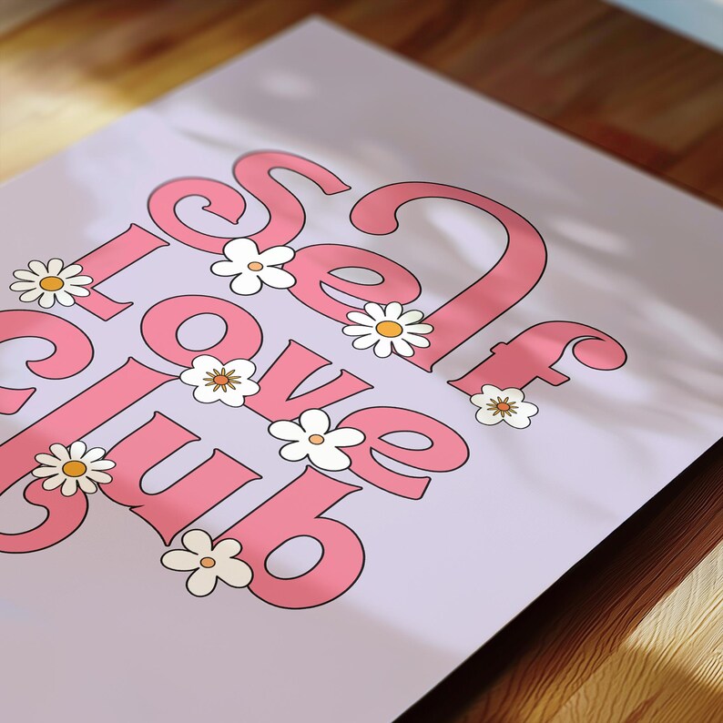 May include: A rectangular print on a light lavender background featuring the pink text "SELF LOVE CLUB" in a bold, rounded font. The design is decorated with several small white daisy flowers with yellow centres scattered among the letters.