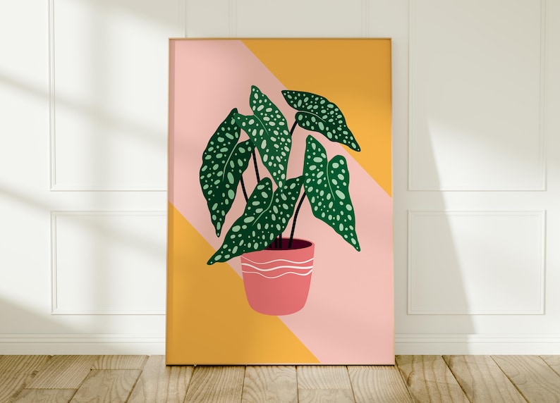 May include: A framed art print depicting a houseplant illustration. The plant has large green leaves with white spots, and is in a pink pot with white stripes. The background is a geometric design of pink and yellow.